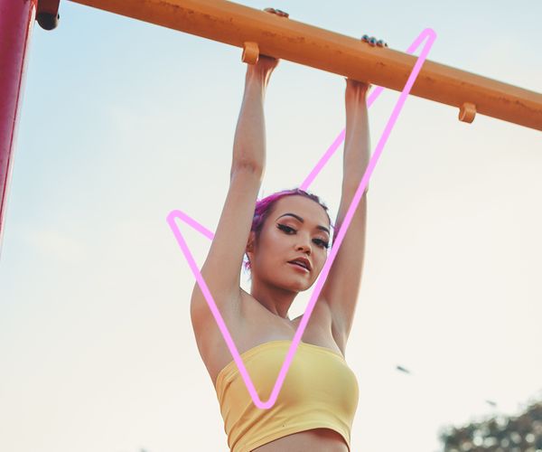 A girl with pink hair hangs from a bar outside with the Sure tick in the background