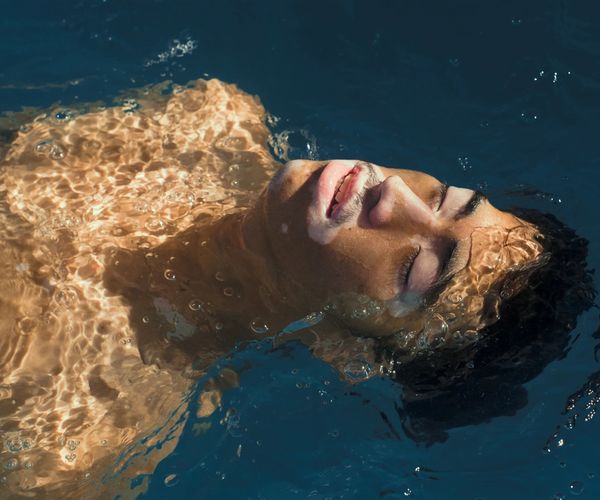 A man lays on his back in a pool with the sun shining on this face