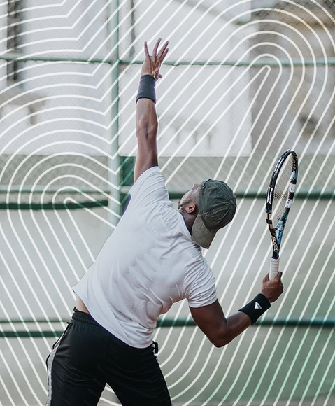 A man with a sweaty back in the middle of a tennis serve 